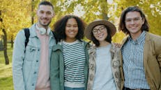 Four friends smiling together in a park during a sunny fall day.