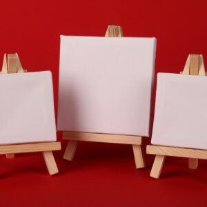 Three small blank art canvases on wooden easels, ready for painting, on a bold red background.