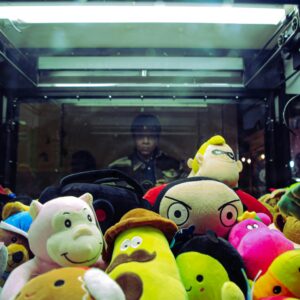 Vibrant plush toys inside a claw machine with a person reflected in the glass.
