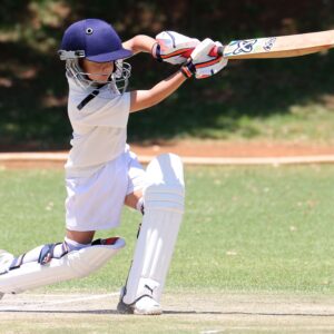 A young boy playing cricket, executing a classic sweep shot on a sunny day.