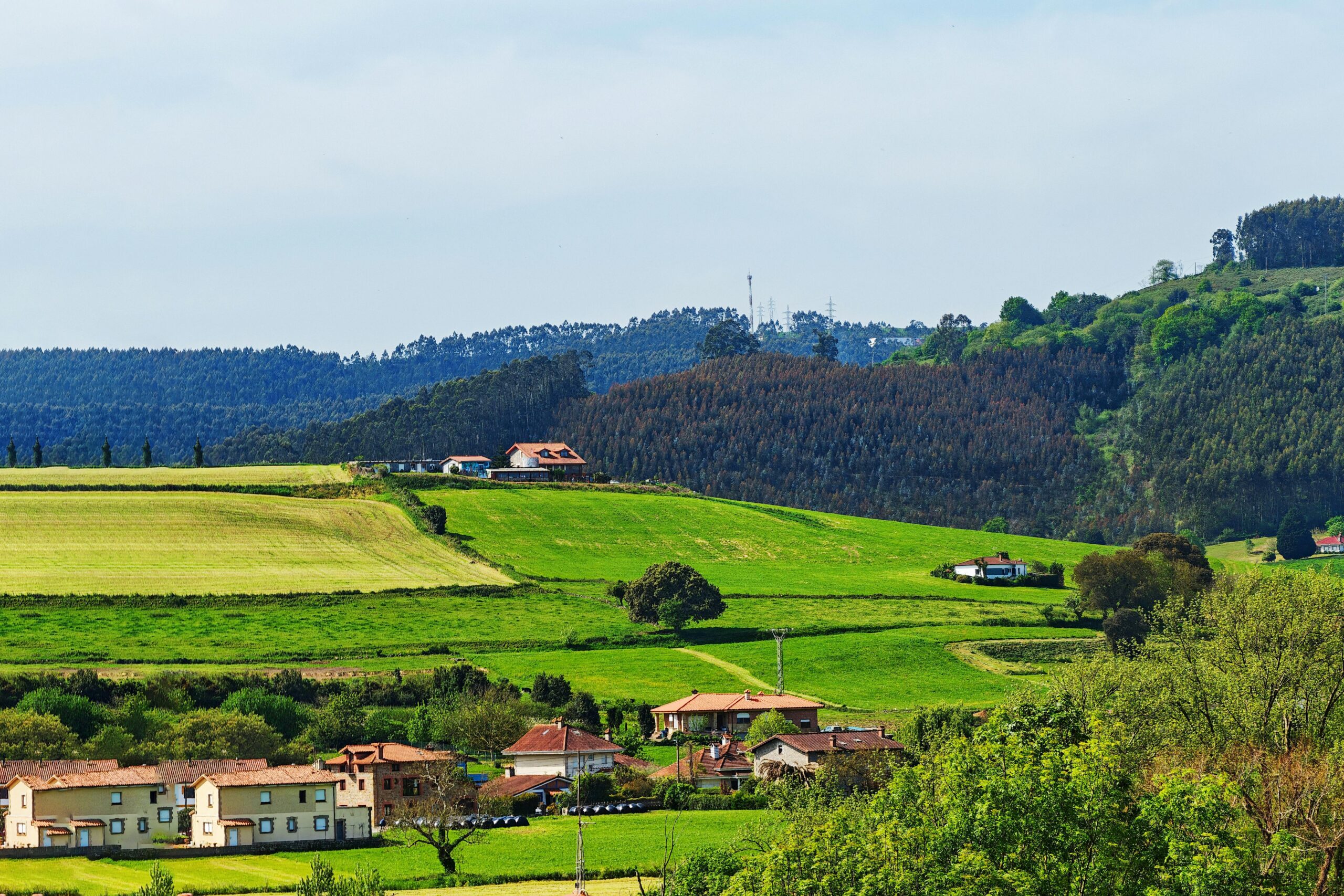 Beautiful green hills with scattered farms and homes under a clear sky.