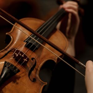 Detailed shot of hands playing a violin, highlighting the strings and bow in a dim setting.