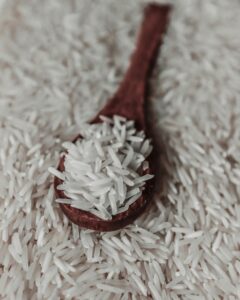 From above of raw white rice grains on wooden spoon placed on pile